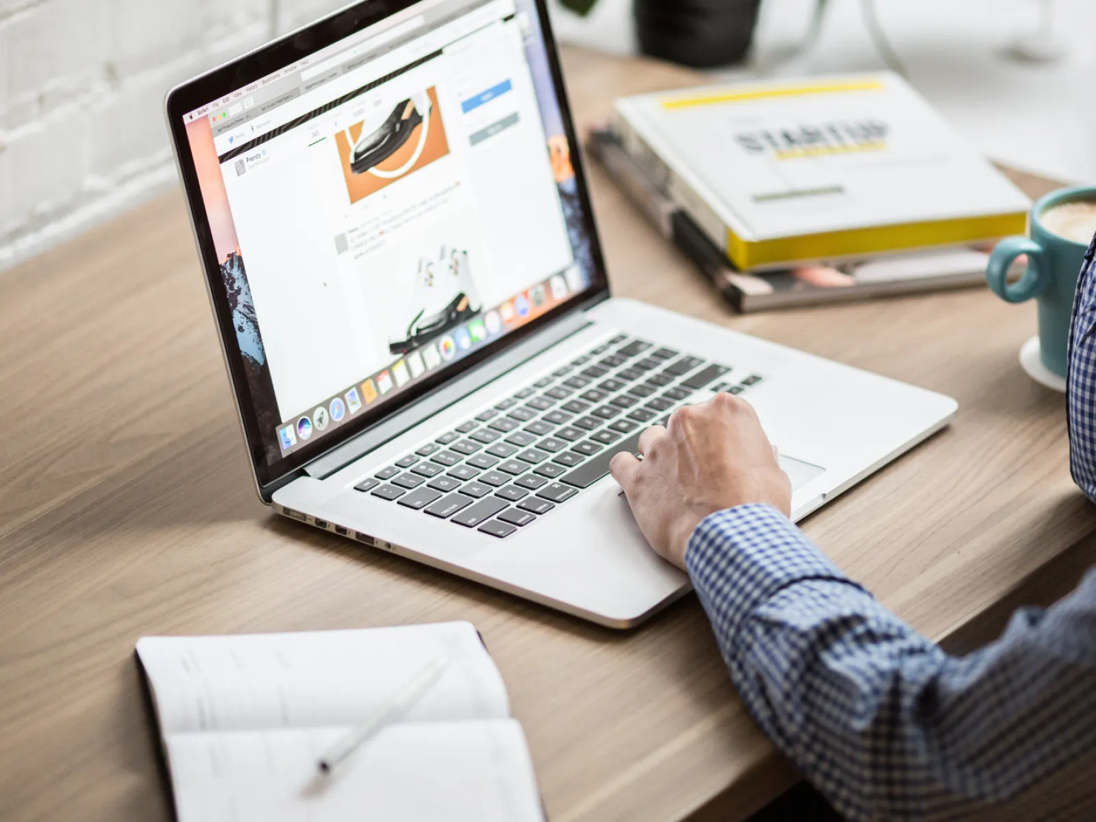 Person using a laptop on a wooden desk with notes and a cup of coffee nearby.