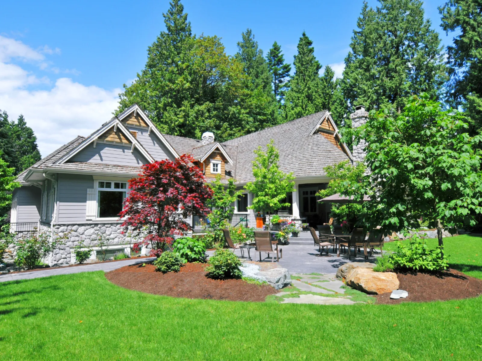 Suburban house with stone and wood exterior surrounded by lush green lawn and vibrant trees on a sunny day