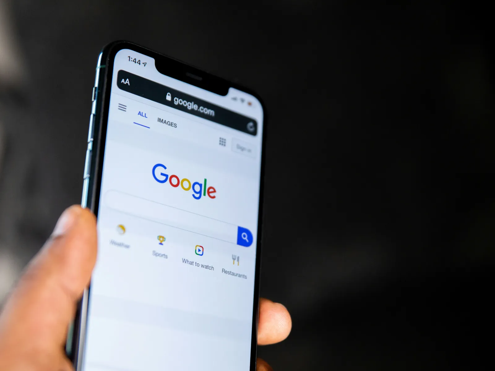 A hand holding a smartphone displaying the Google homepage with search bar and results.