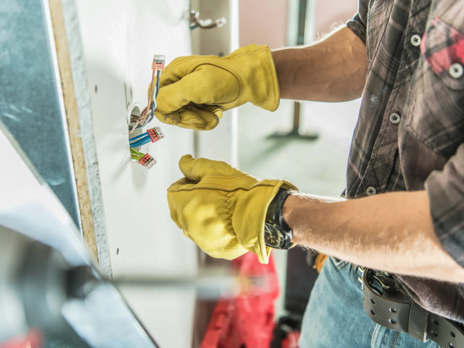 Hands in yellow gloves connecting electrical wires in a home improvement setting.