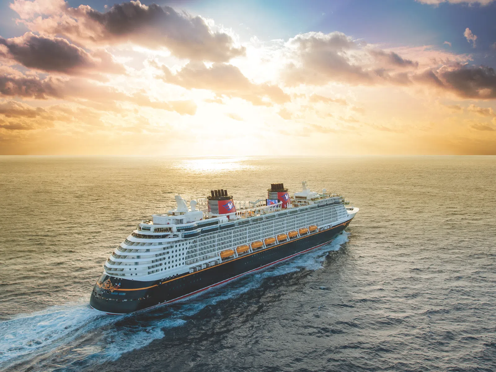 Large cruise ship sailing on calm ocean waters during a scenic sunset with partially cloudy sky.