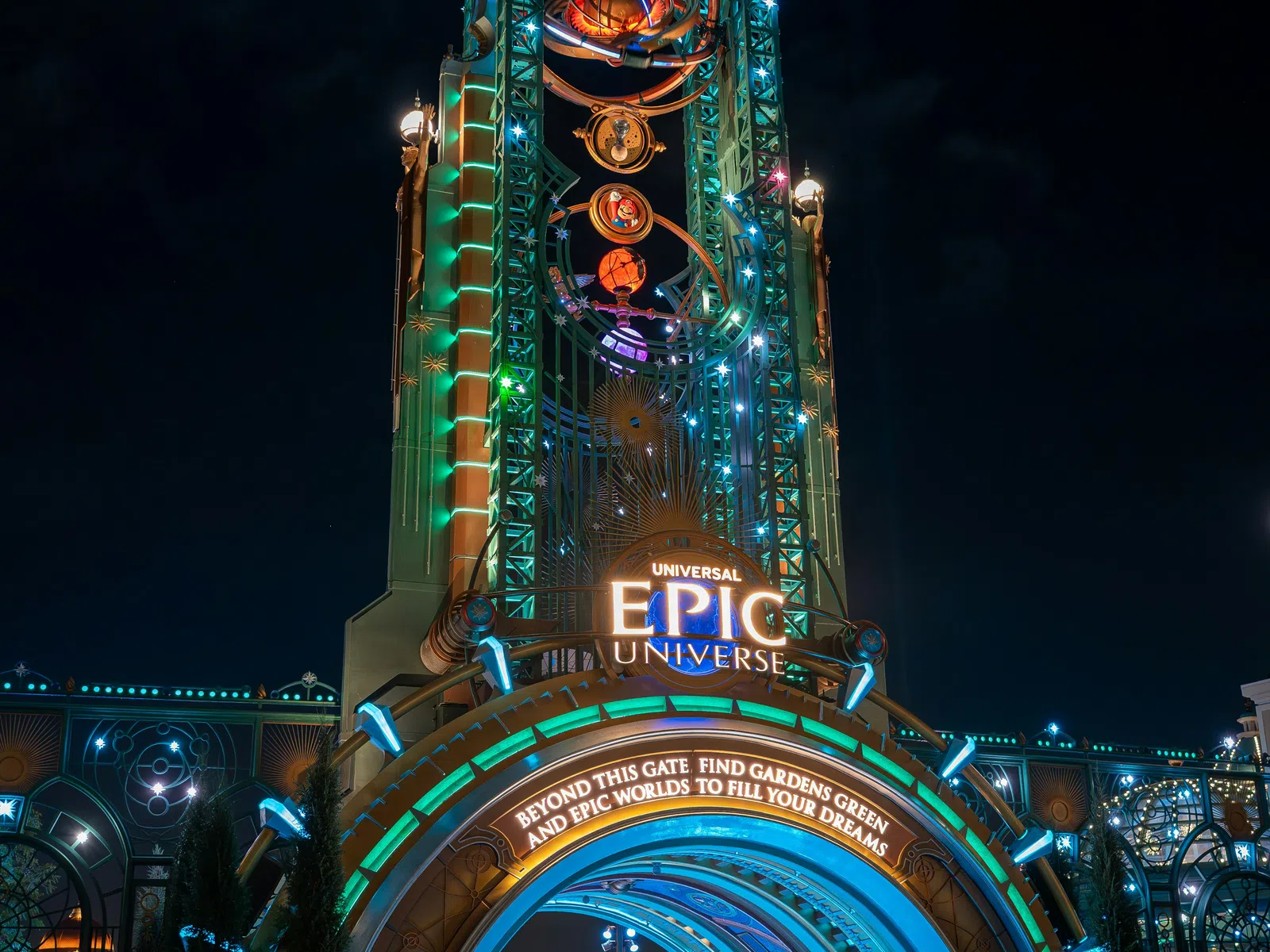 Universal Epic Universe entrance gate illuminated at night with colorful lights and visitors walking through.