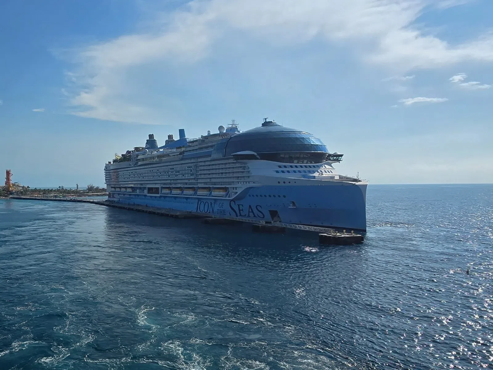 Large cruise ship sailing near a coast under a clear blue sky with calm ocean waters.