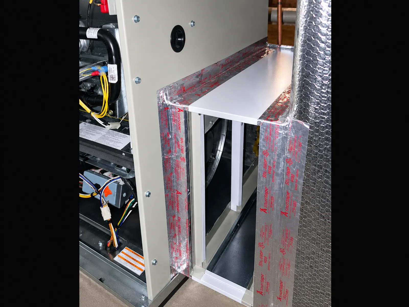 Close-up of a furnace with silver insulation tape sealing ductwork and electrical wiring visible inside.