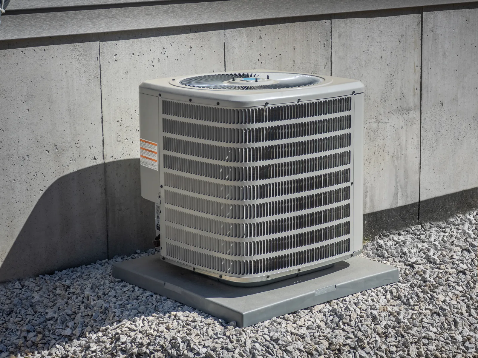 Outdoor central air conditioning unit installed on a concrete pad beside a building wall over gravel bed