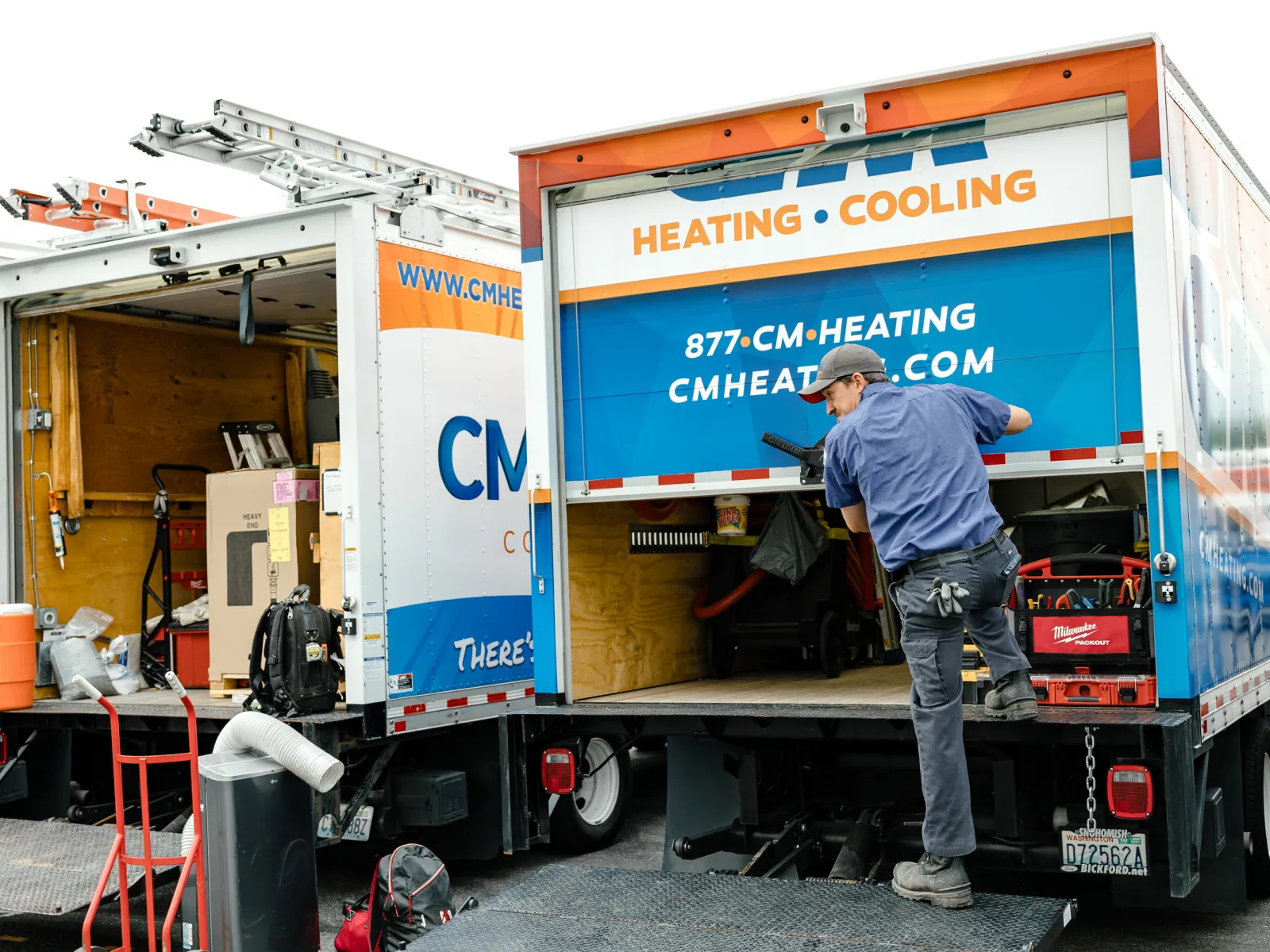 Technician loading HVAC equipment into CM Heating and Cooling service truck with tools and ladders visible.