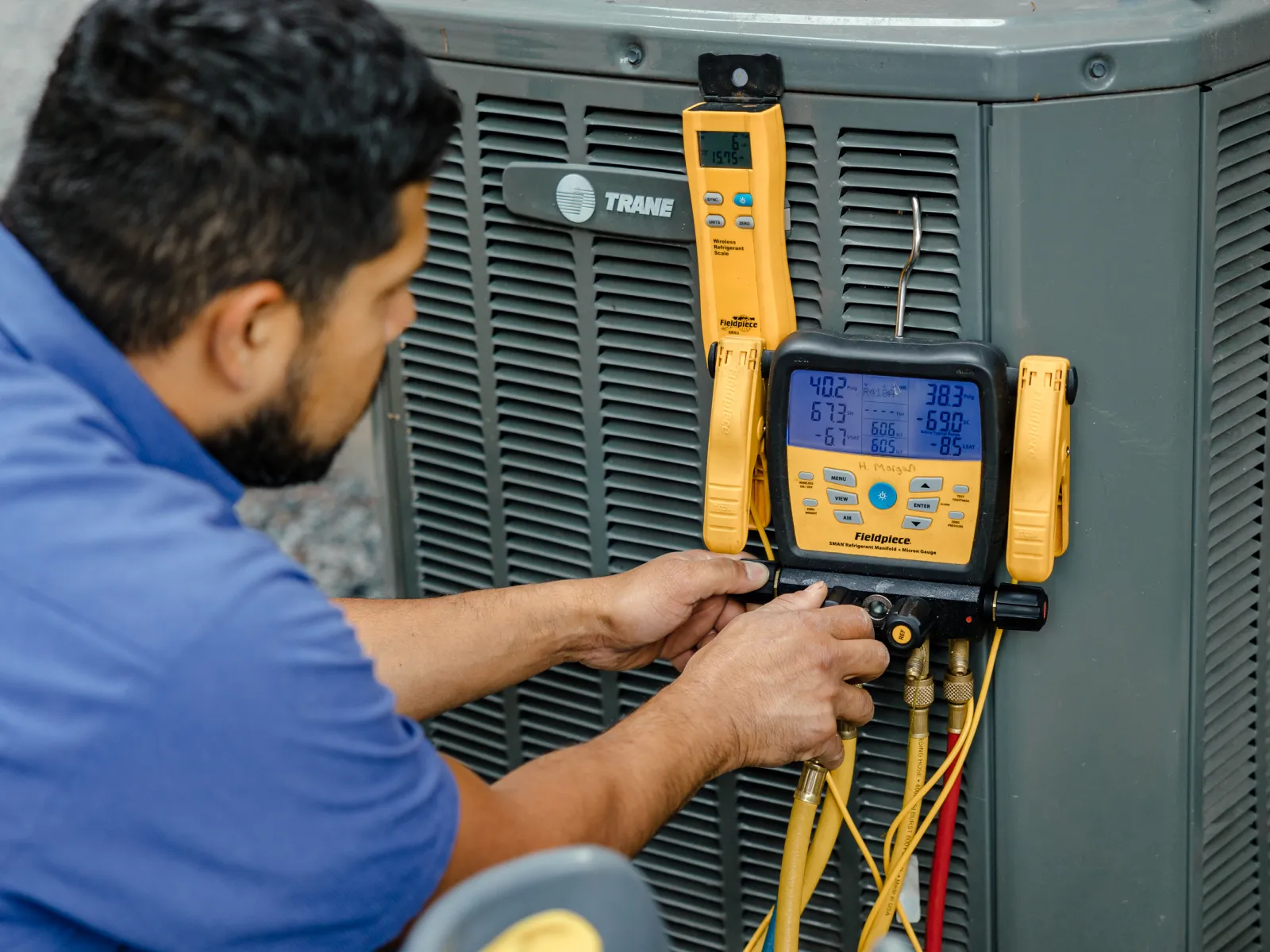 Technician servicing Trane air conditioning unit using yellow digital manifold gauge set outdoors