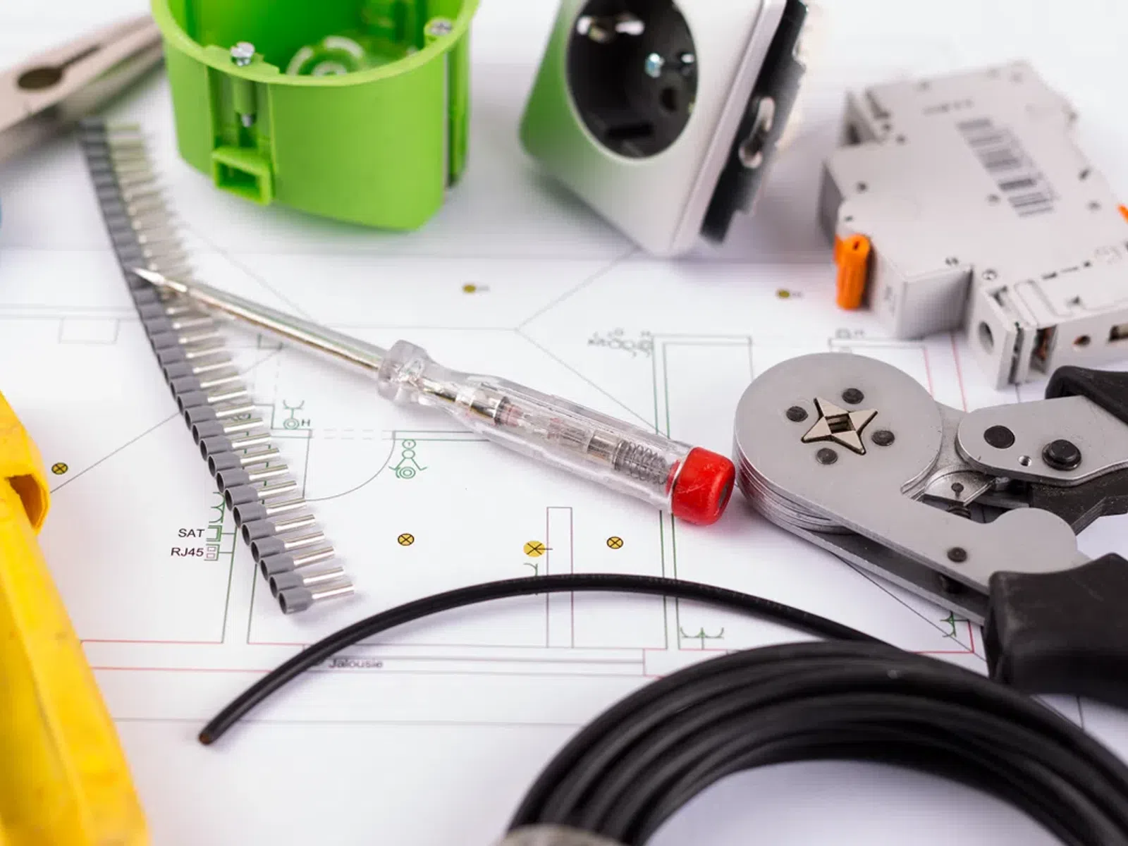 Electrical tools and components on a blueprint including pliers, wire strippers, screwdriver, and wiring parts.