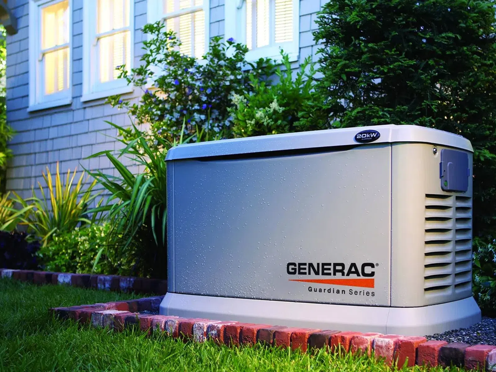 Generac Guardian Series home backup generator installed outside a house with landscaping at dusk.