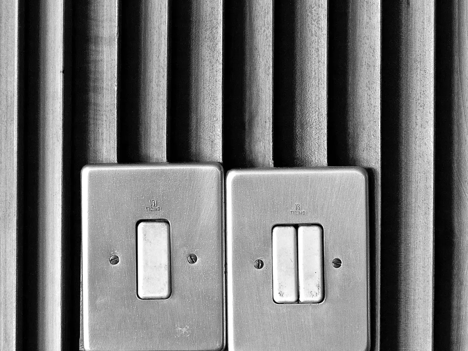 Metallic light switches on a wall with vertical ridged texture in black and white.