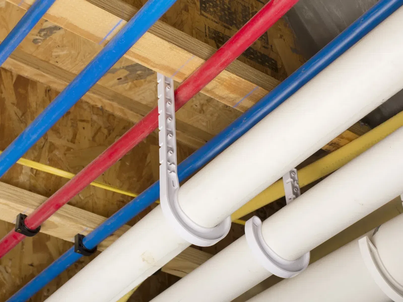 Color-coded blue, red, and white plumbing pipes mounted on wooden ceiling framework in building construction