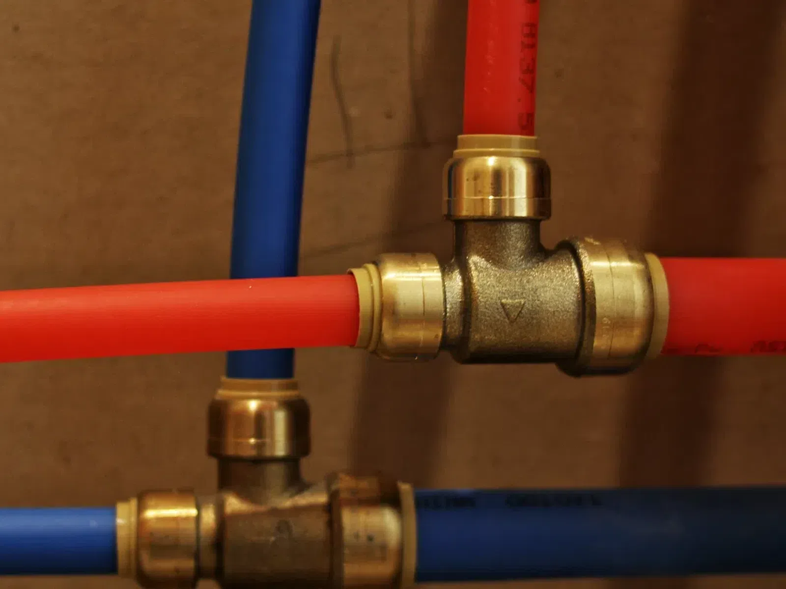 Close-up of red and blue plastic pipes connected with brass fittings on a brown background.