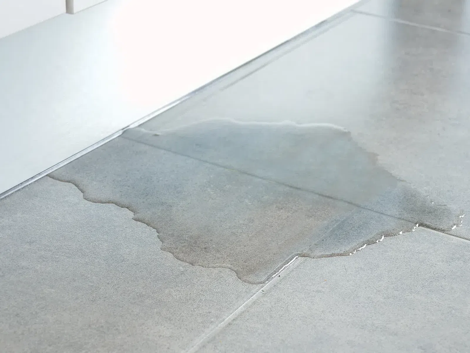 Water spill on gray tiled floor near white cabinet edge indoors