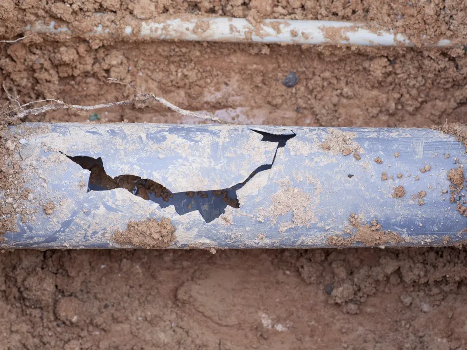 Cracked damaged underground plastic pipe exposed in dirt trench during repair work