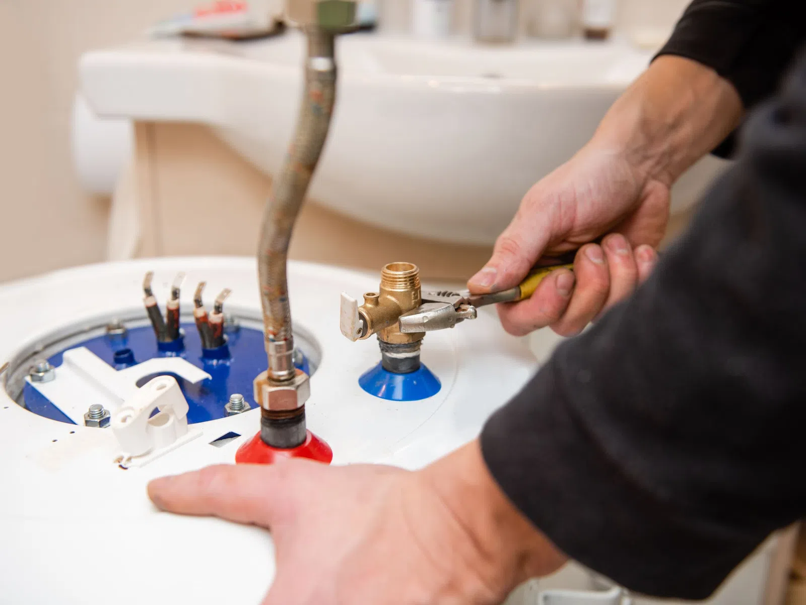 Plumber tightening a valve on a water heater with a wrench in a residential bathroom setting