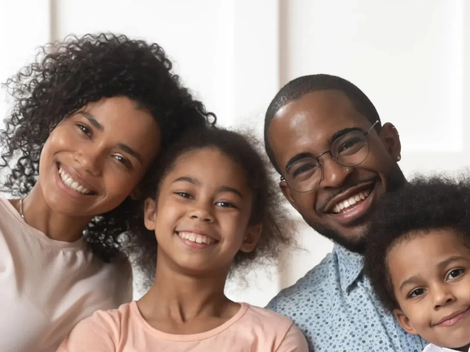 Smiling family of four sitting closely together wearing casual clothes in a bright room.