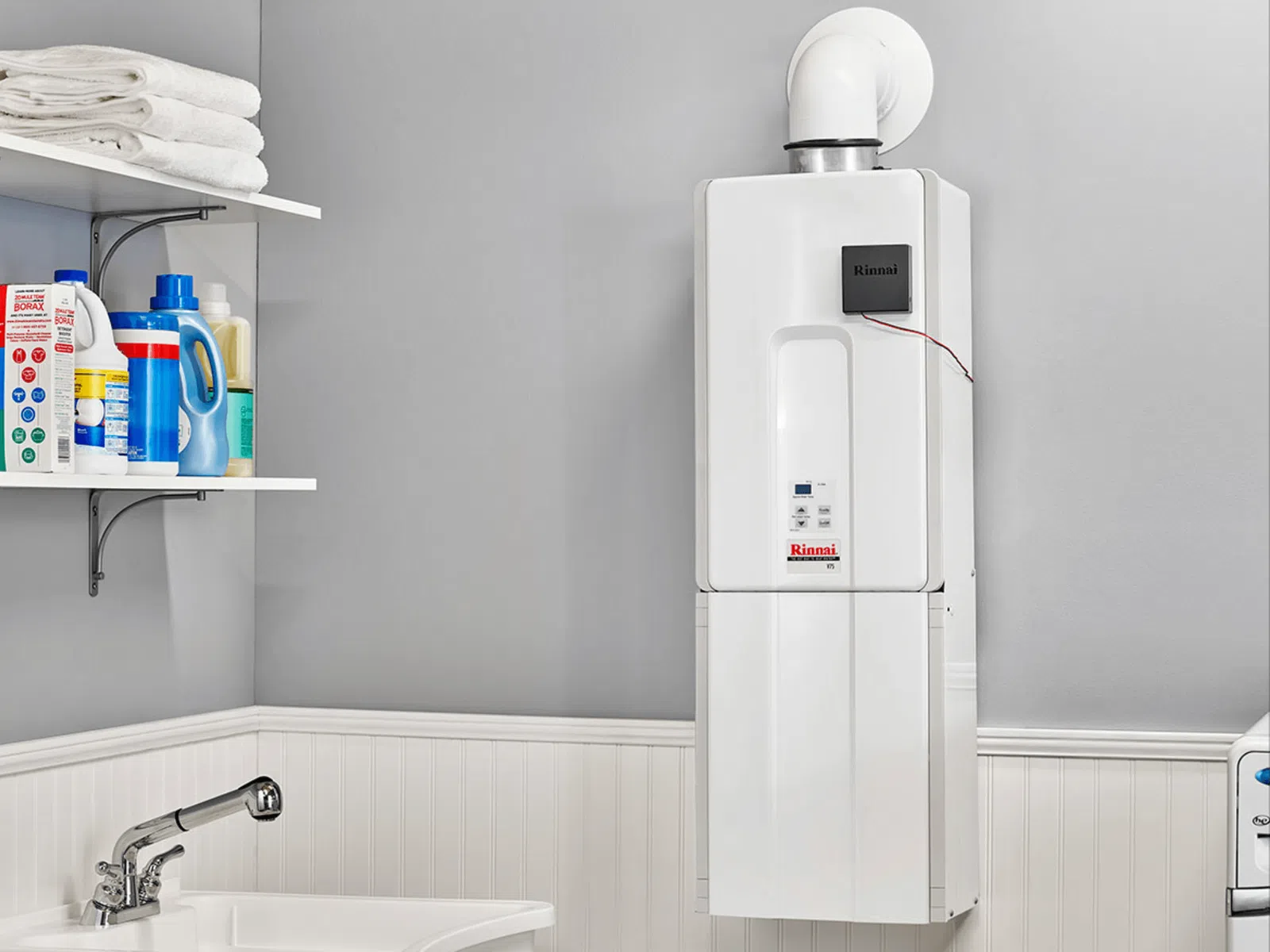 White tankless water heater mounted on a gray wall above white wainscoting in a laundry room