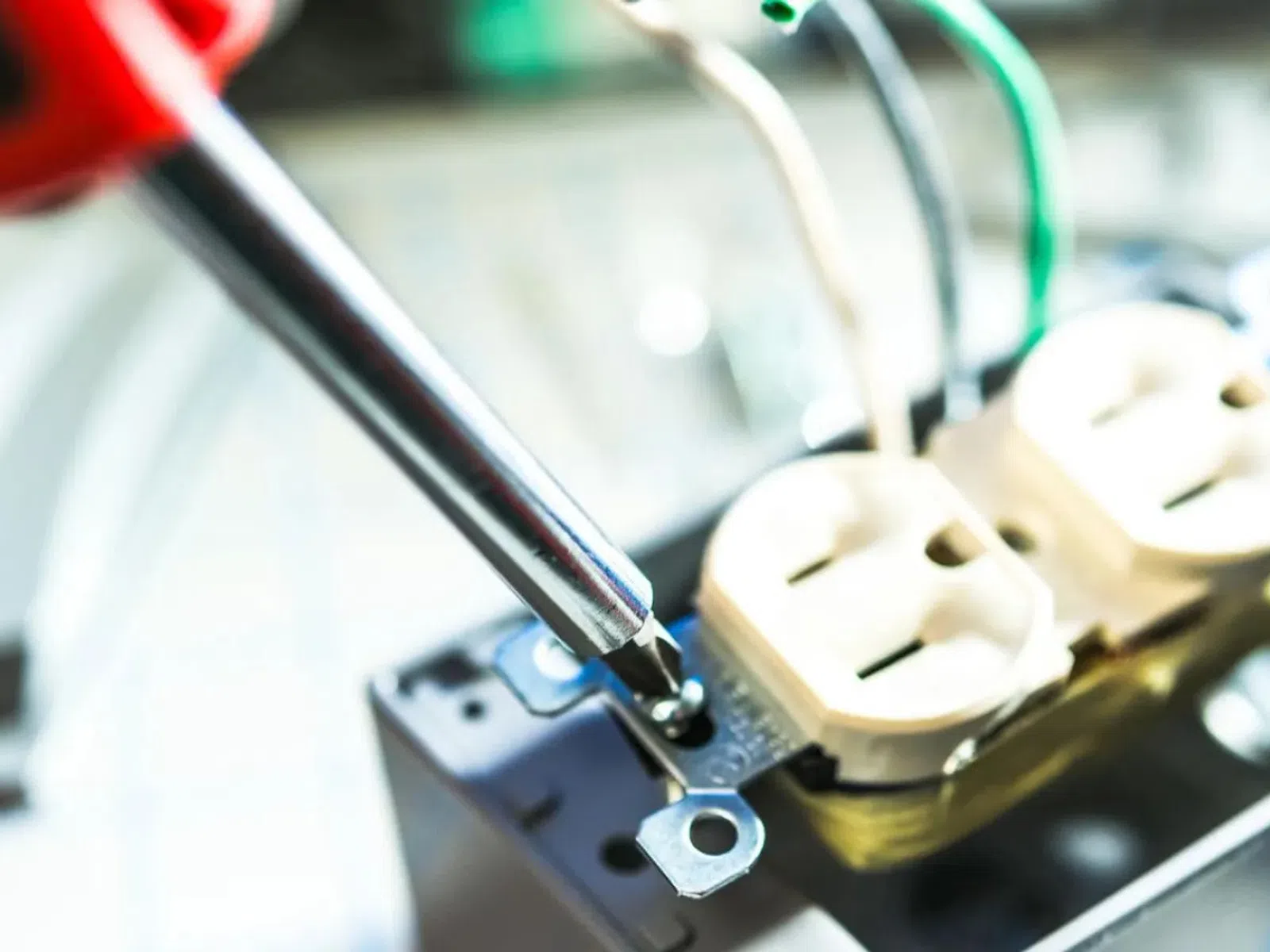 Close-up of screwdriver tightening screws on an electrical outlet in a metal junction box.