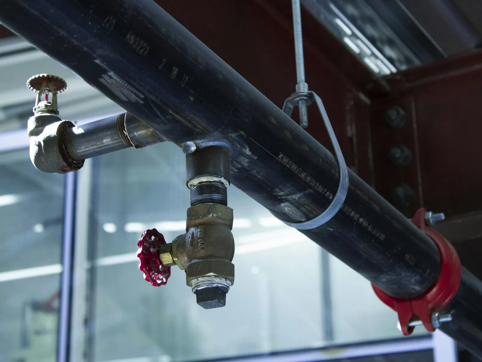Industrial black pipeline with red valves and metal clamps inside a commercial building ceiling.