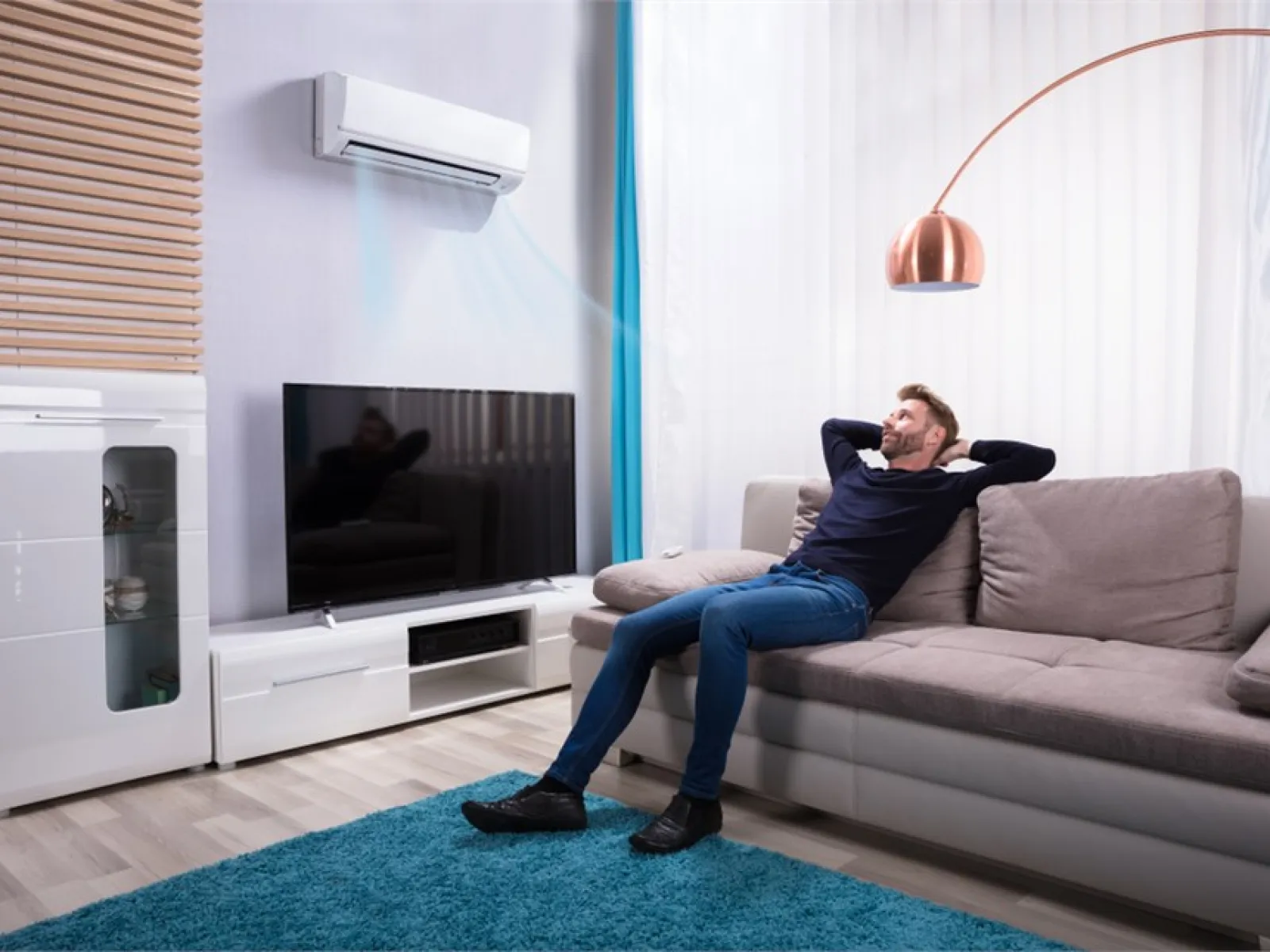 Man sitting relaxed on sofa in living room with air conditioner blowing cool air and modern decor.