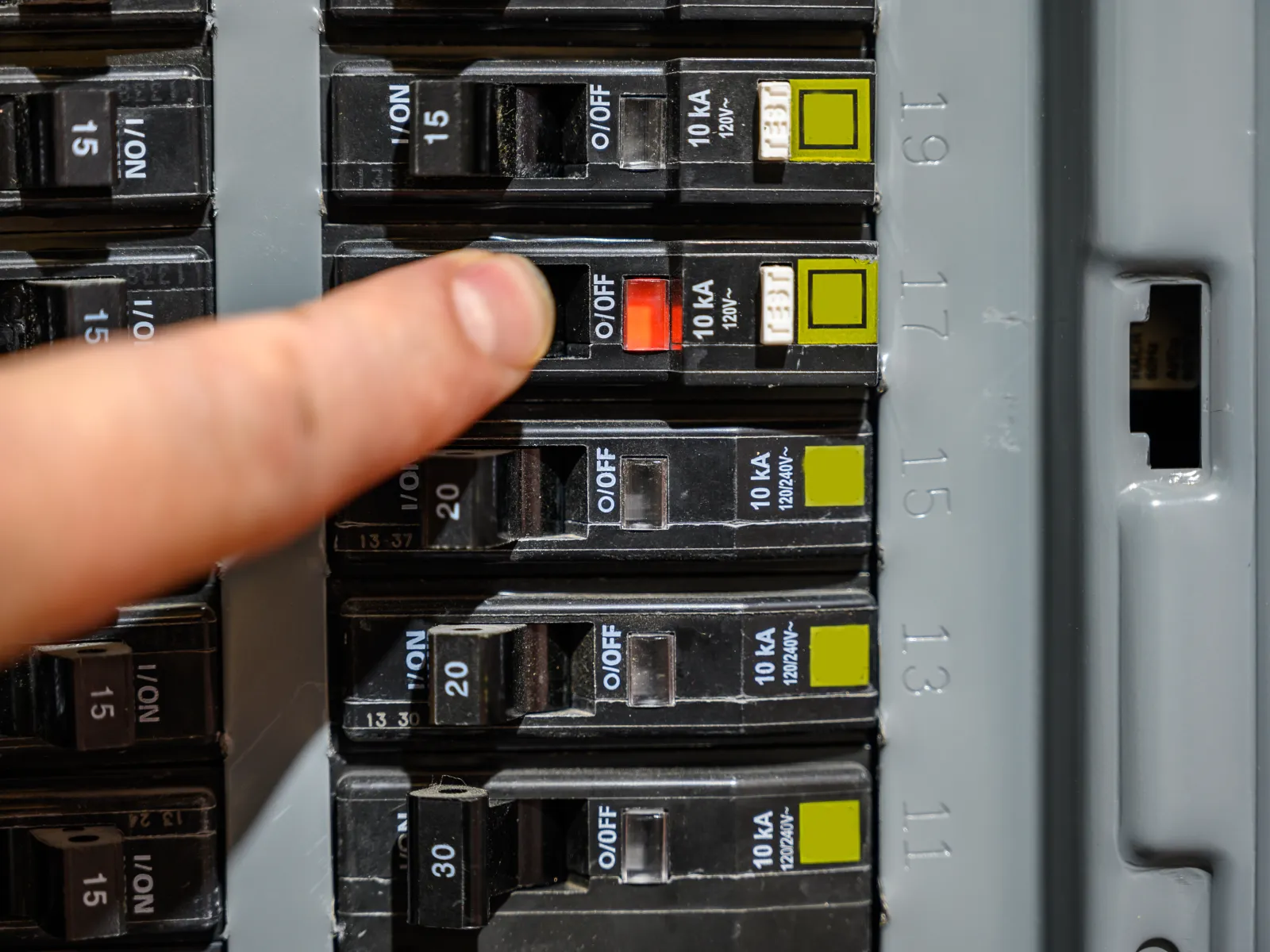 Hand turning off a circuit breaker switch in an electrical panel for safety or maintenance.