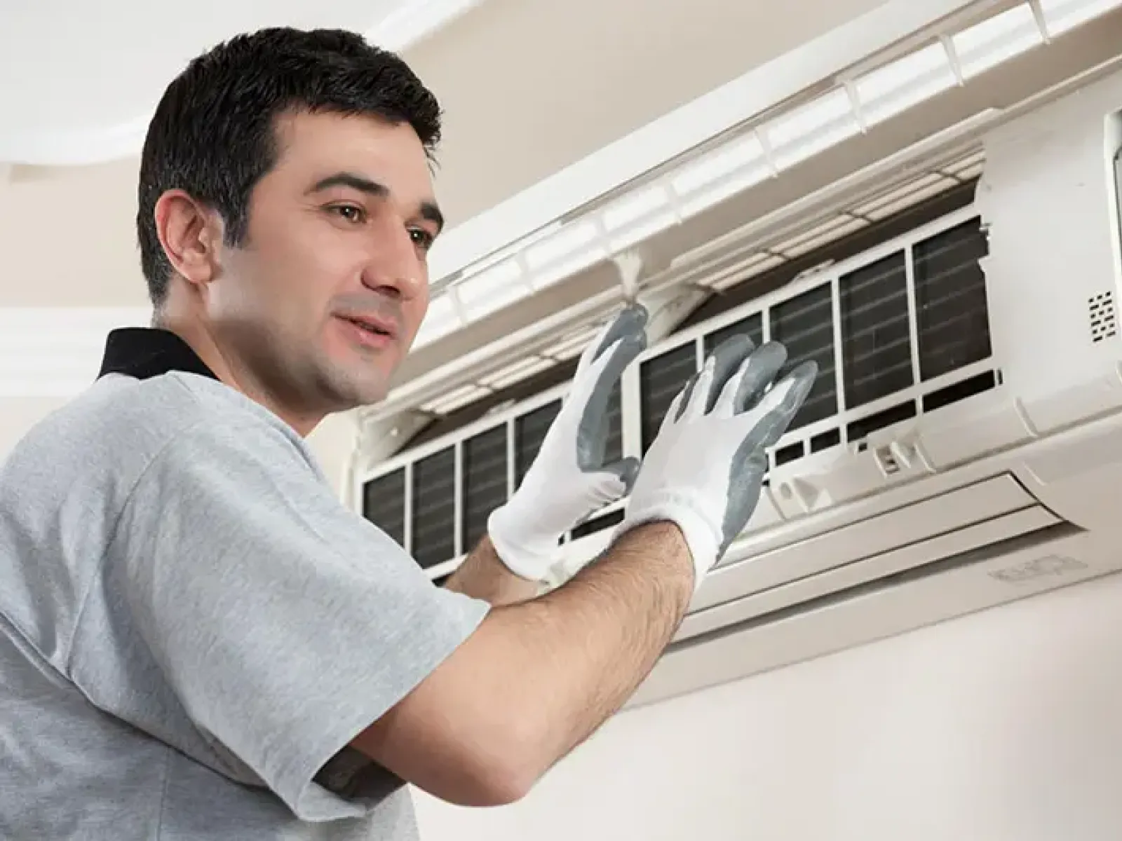 Technician wearing gloves repairing or inspecting a wall-mounted air conditioning unit indoors.