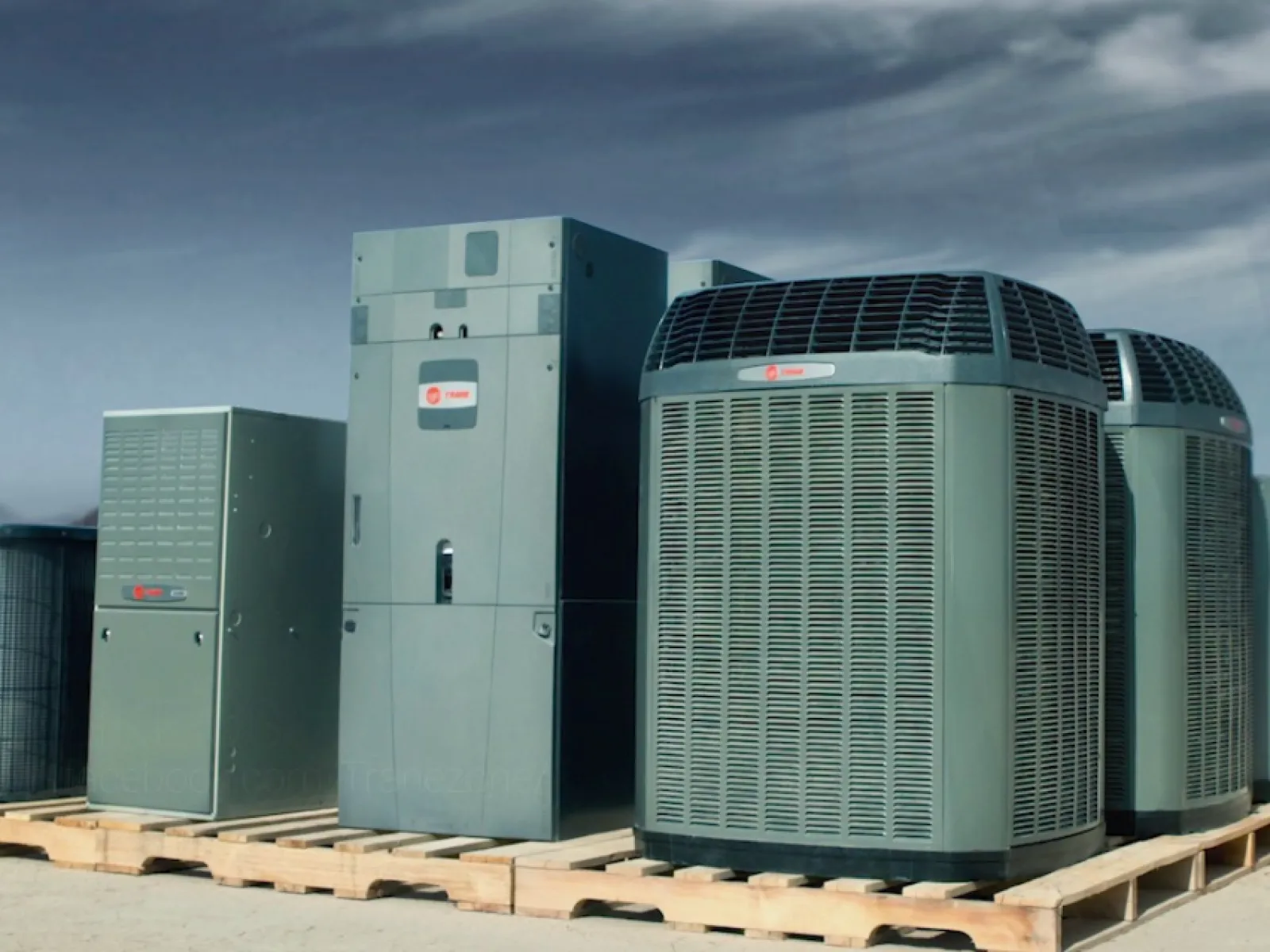 Multiple Trane air conditioning and HVAC units displayed on wooden pallets outdoors under a cloudy sky.