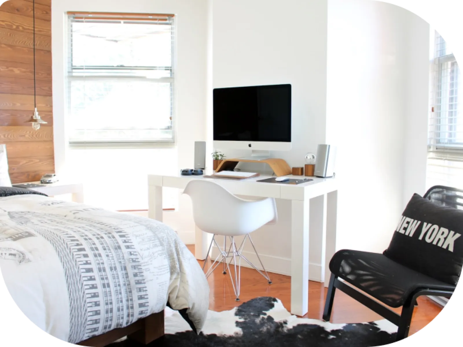 Bright bedroom with white modern desk, computer, cozy bed, New York pillow, and natural light from windows.
