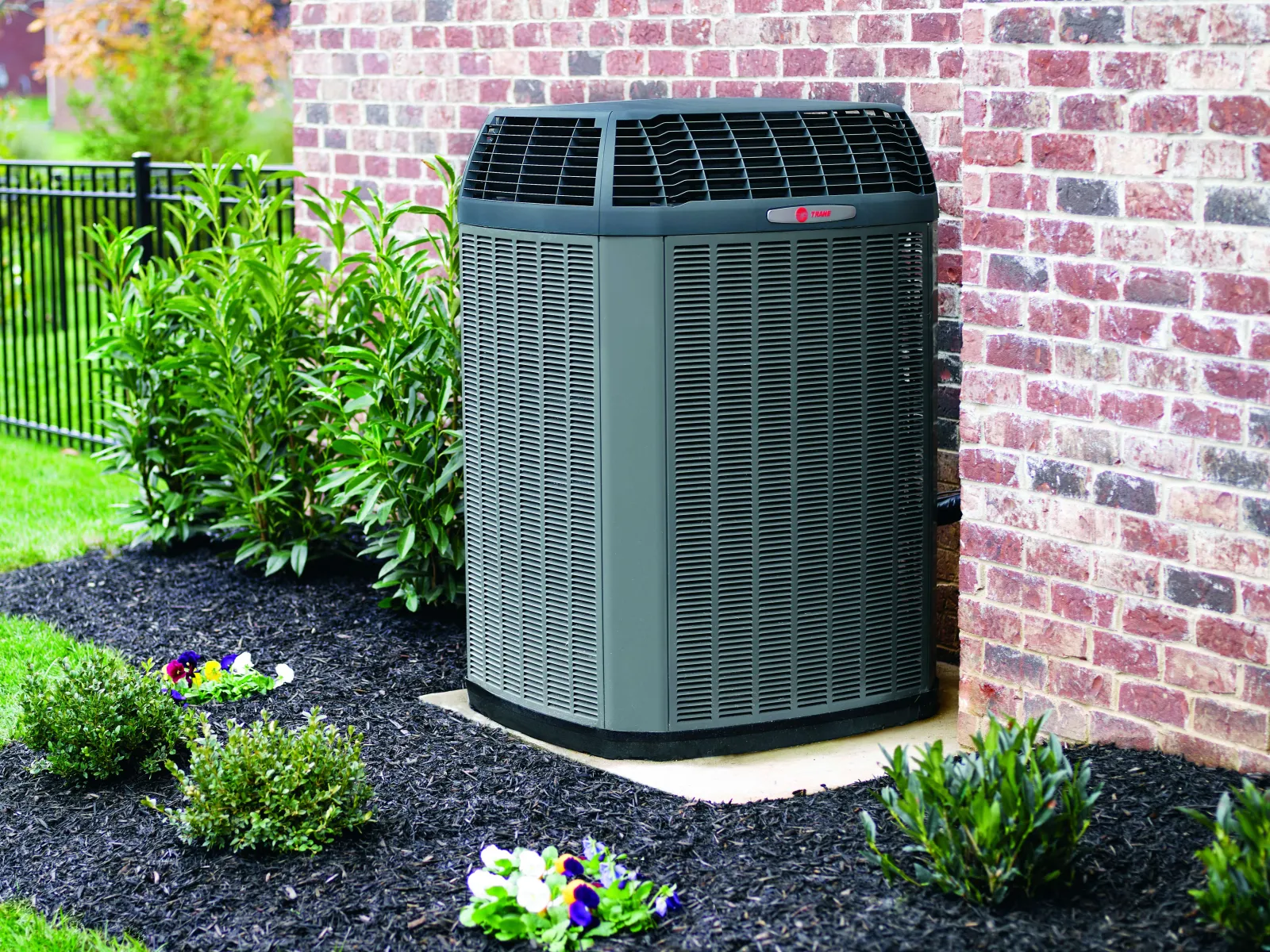 Modern outdoor air conditioning unit installed beside brick house wall with landscaped garden.