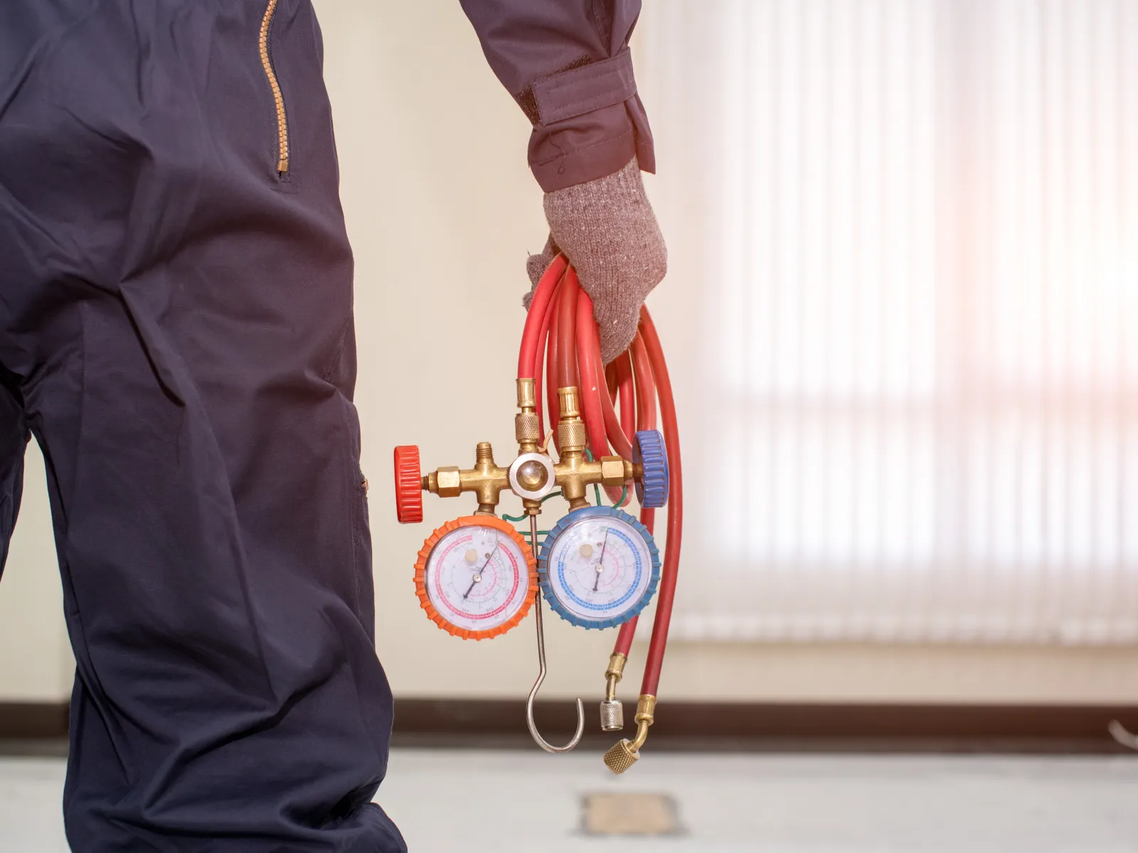 Technician holding red refrigerant hoses with pressure gauges for HVAC system maintenance indoors.
