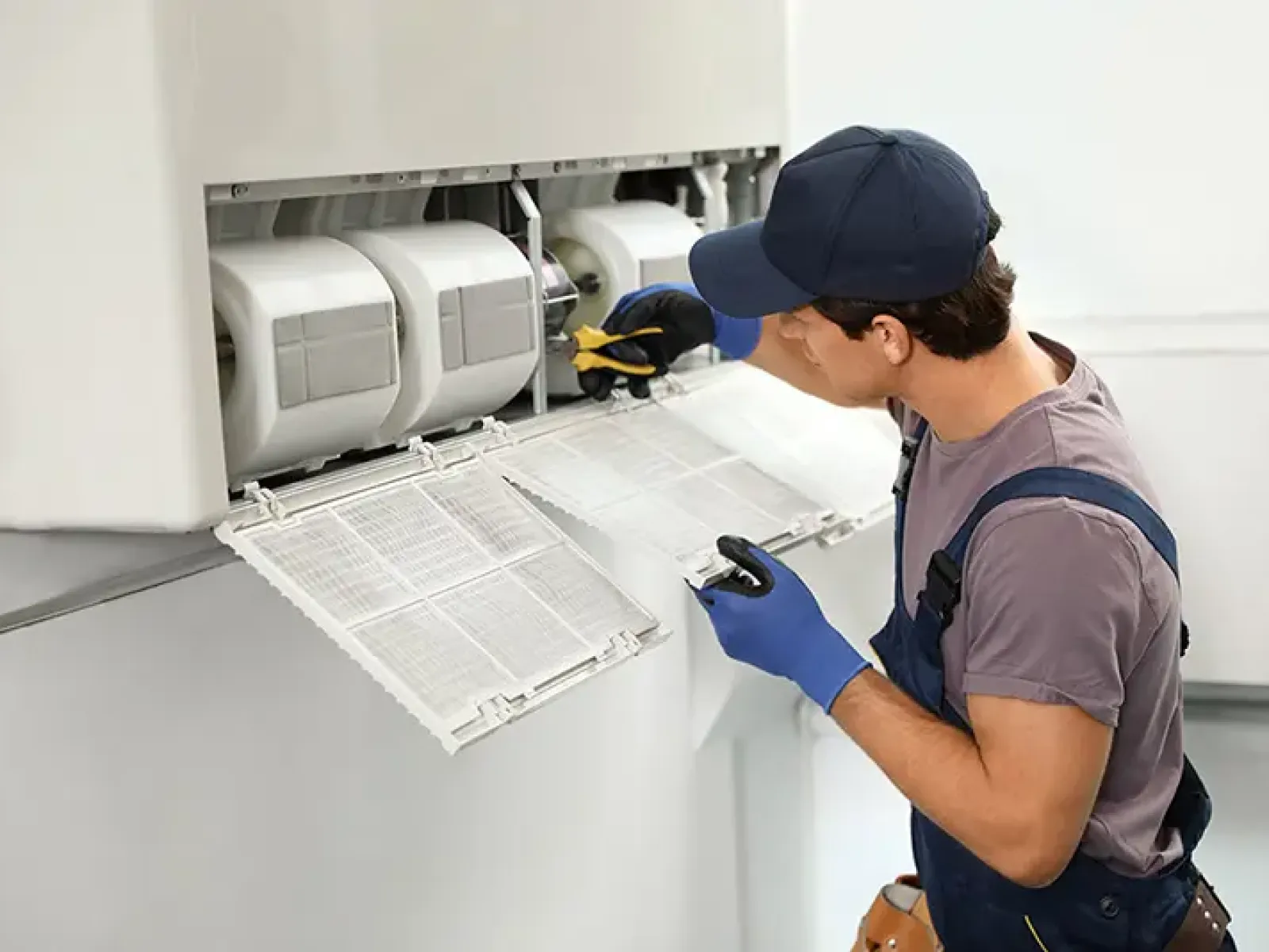 Technician cleaning or repairing the filter and components of an air conditioning unit indoors.