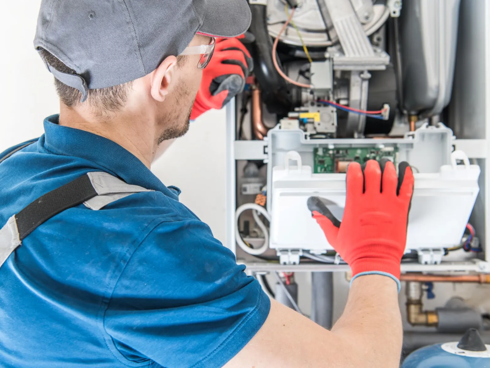 Technician in blue uniform and red gloves repairing or inspecting a boiler or HVAC system indoors.