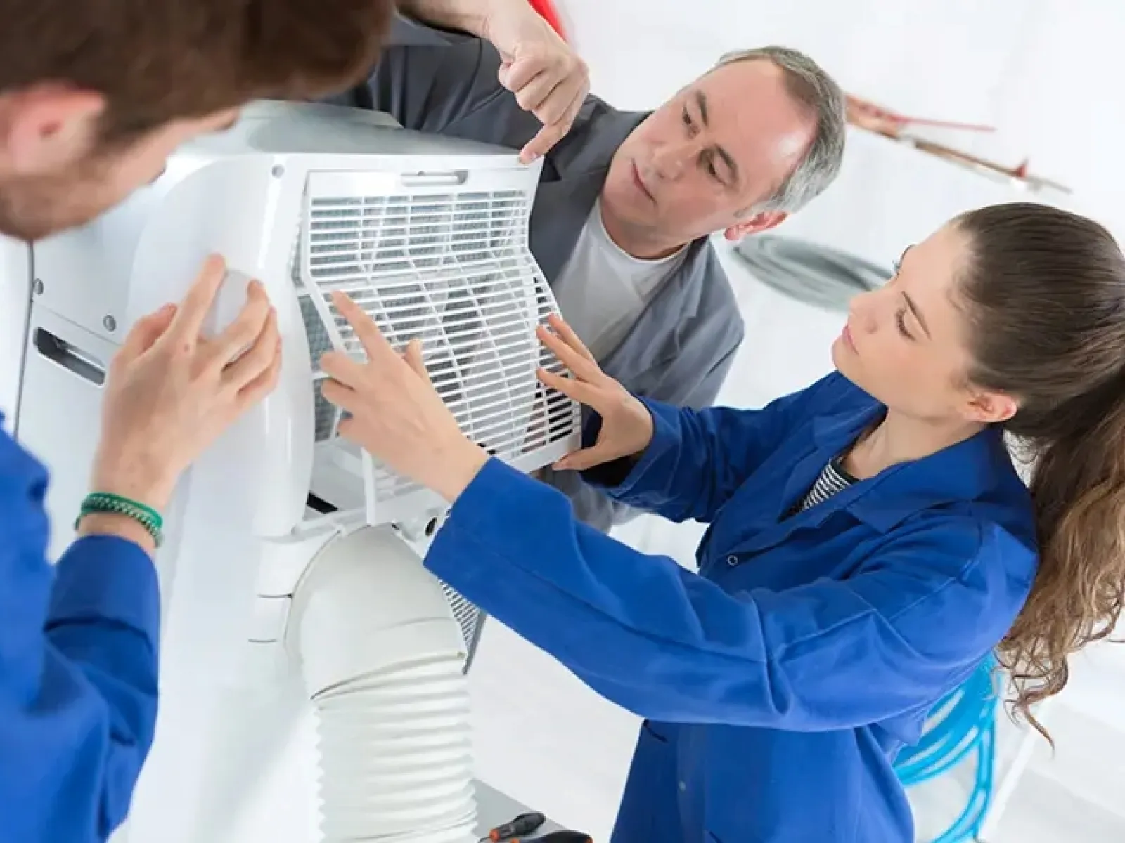 Technicians in blue uniforms repairing and installing a portable air conditioner unit indoors with tools.