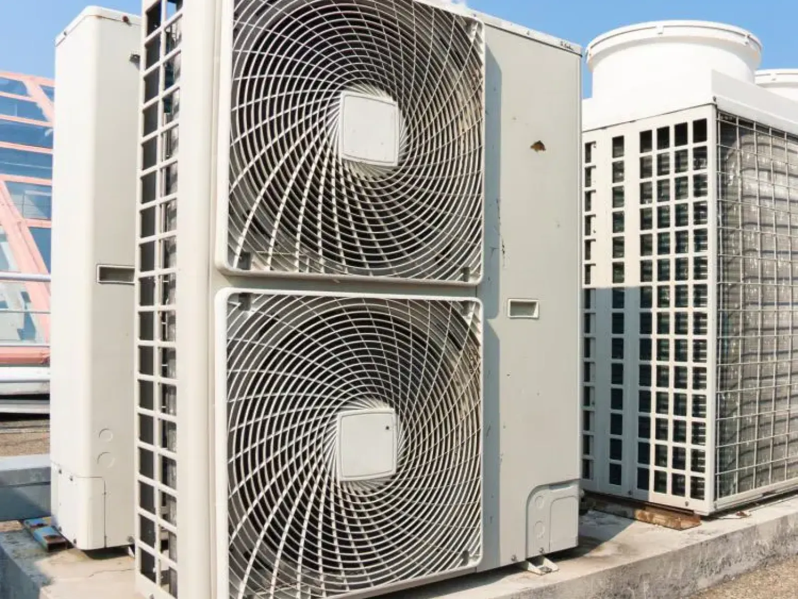Large commercial air conditioning units with circular fan grills installed on a rooftop under a clear sky.