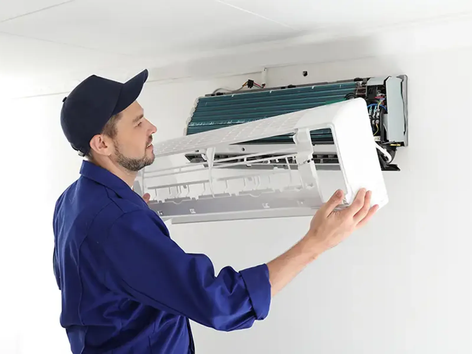Technician in blue uniform repairing or installing a wall-mounted air conditioning unit indoors.