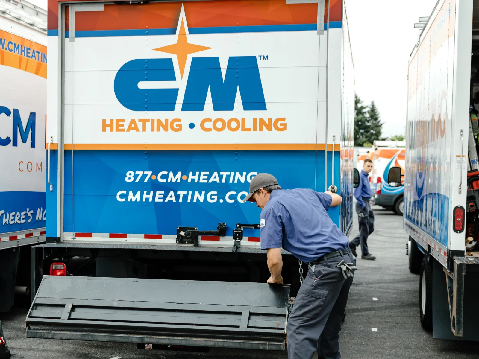 Technician unloading equipment from CM Heating and Cooling service truck in a parking lot with company logos visible.