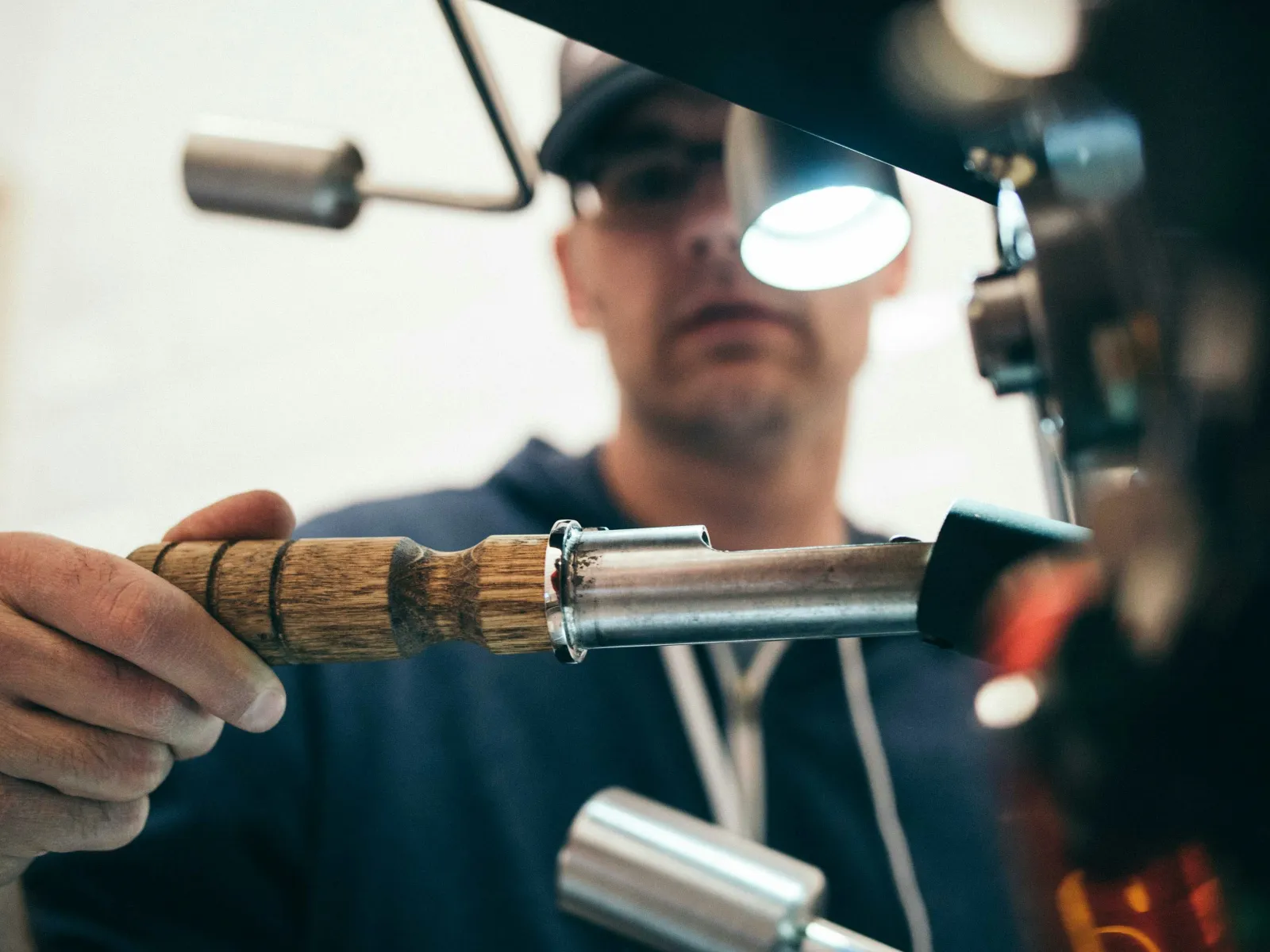 Barista using a wooden-handled portafilter with a professional espresso machine in a cafe setting.