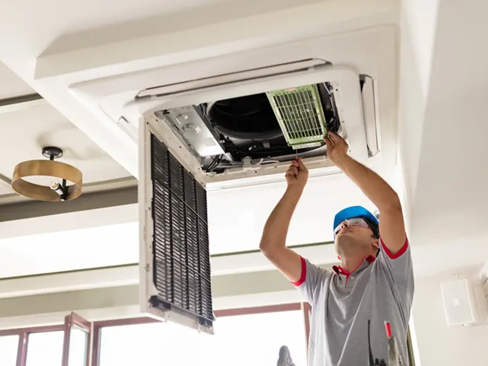 Technician repairing a ceiling air conditioning unit with tools in a modern living room setting