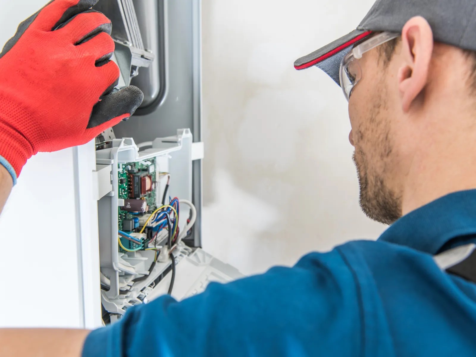 Technician wearing red gloves repairs and inspects electrical appliance circuit board closely indoors.