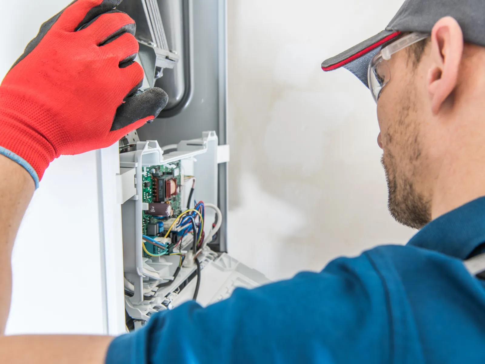 Technician wearing red gloves repairs and inspects electrical appliance circuit board closely indoors.