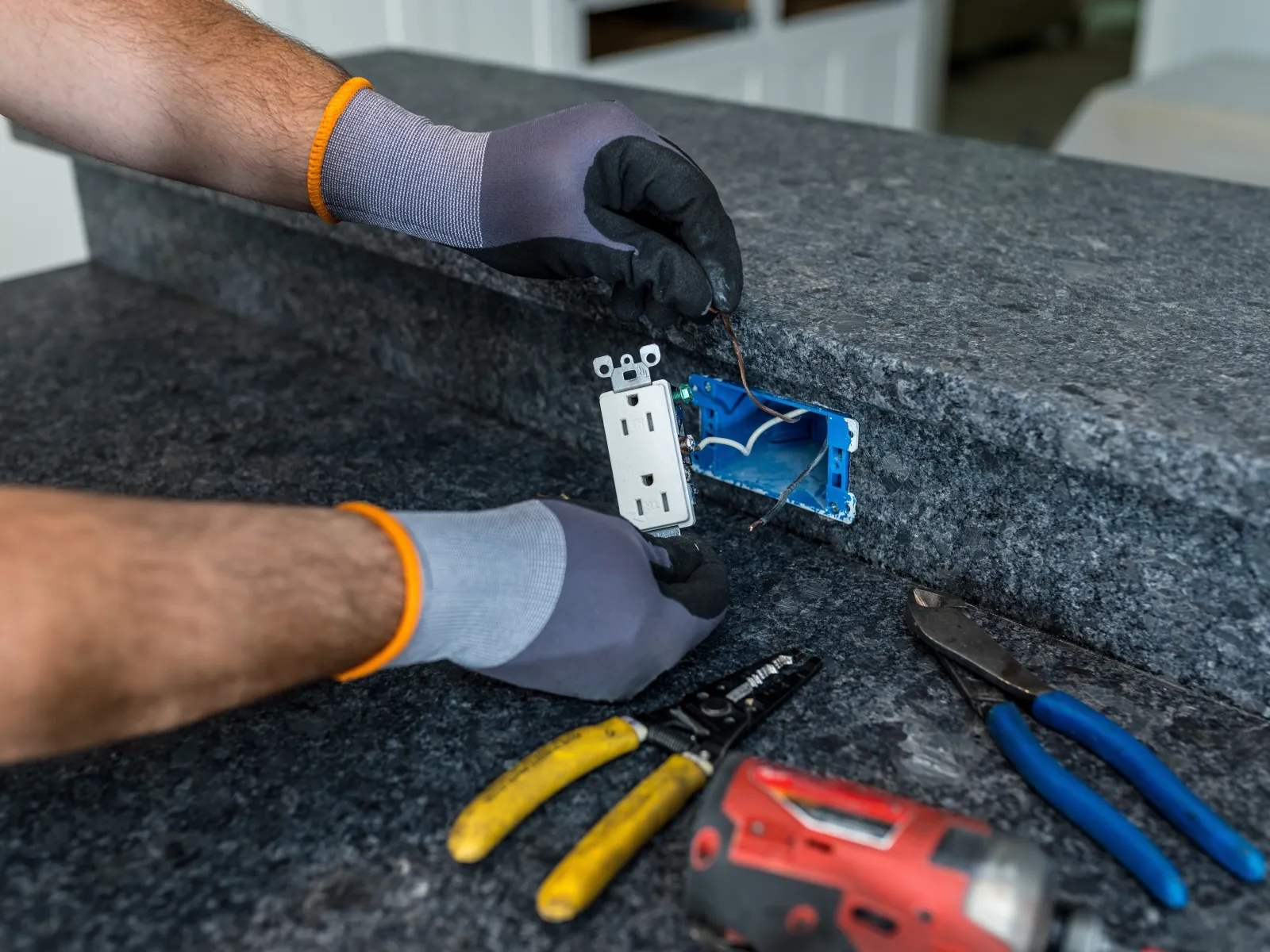 Person using a screwdriver to install or repair a wall electrical outlet with visible red and black wires.