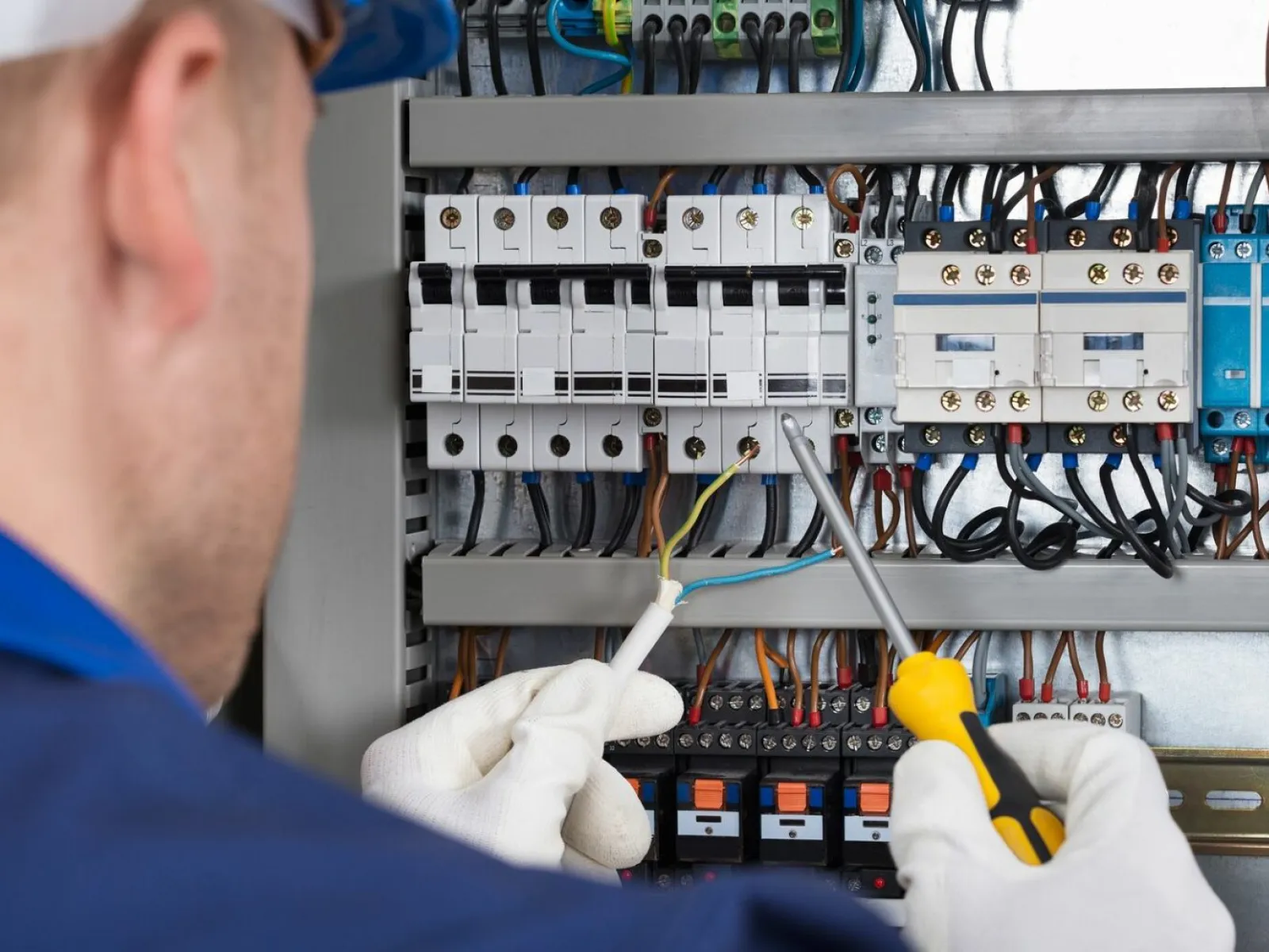 Electrician wearing gloves working on circuit breakers inside an electrical panel with tools and wires.