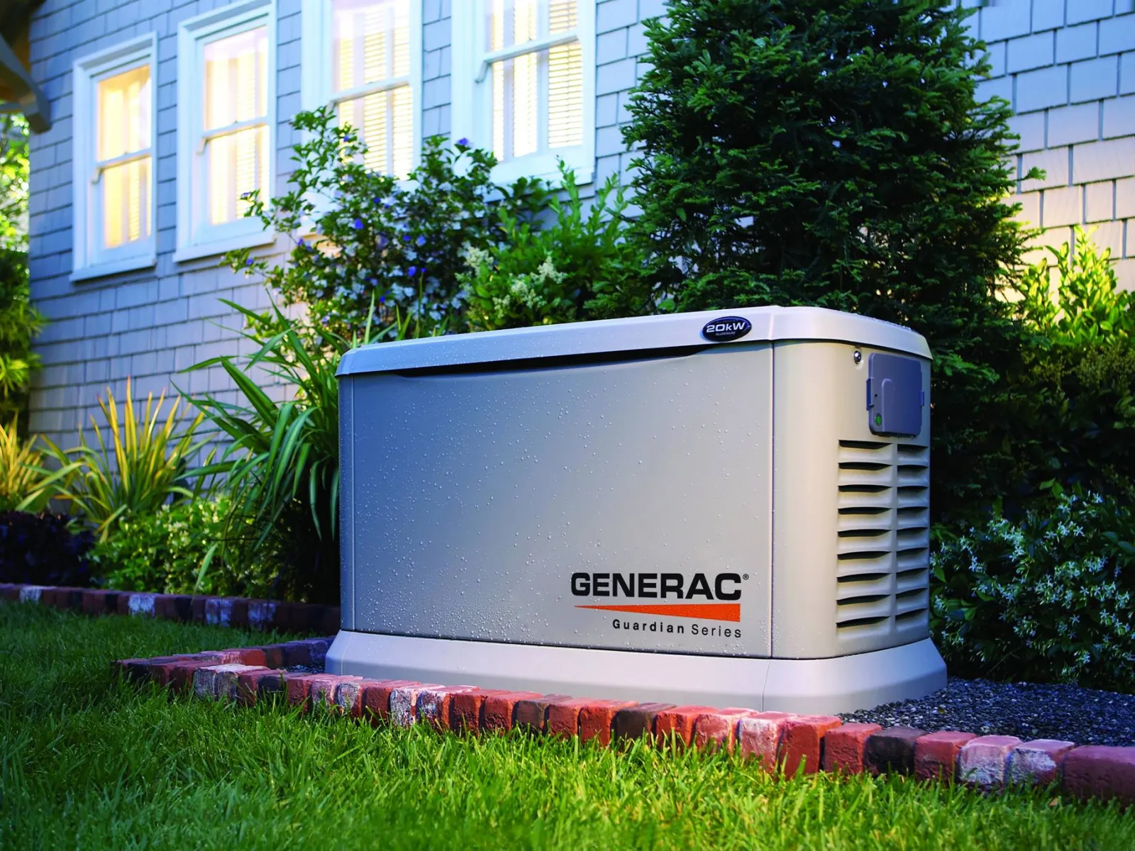 Generac Guardian Series home standby generator installed outdoors next to a house with plants and grass.