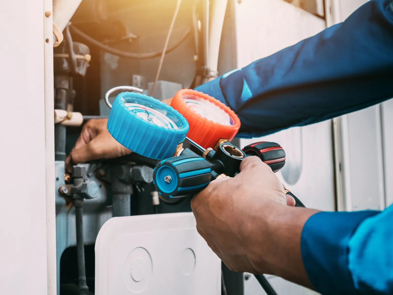 Technician using HVAC gauges to check air conditioning system pressure during maintenance work