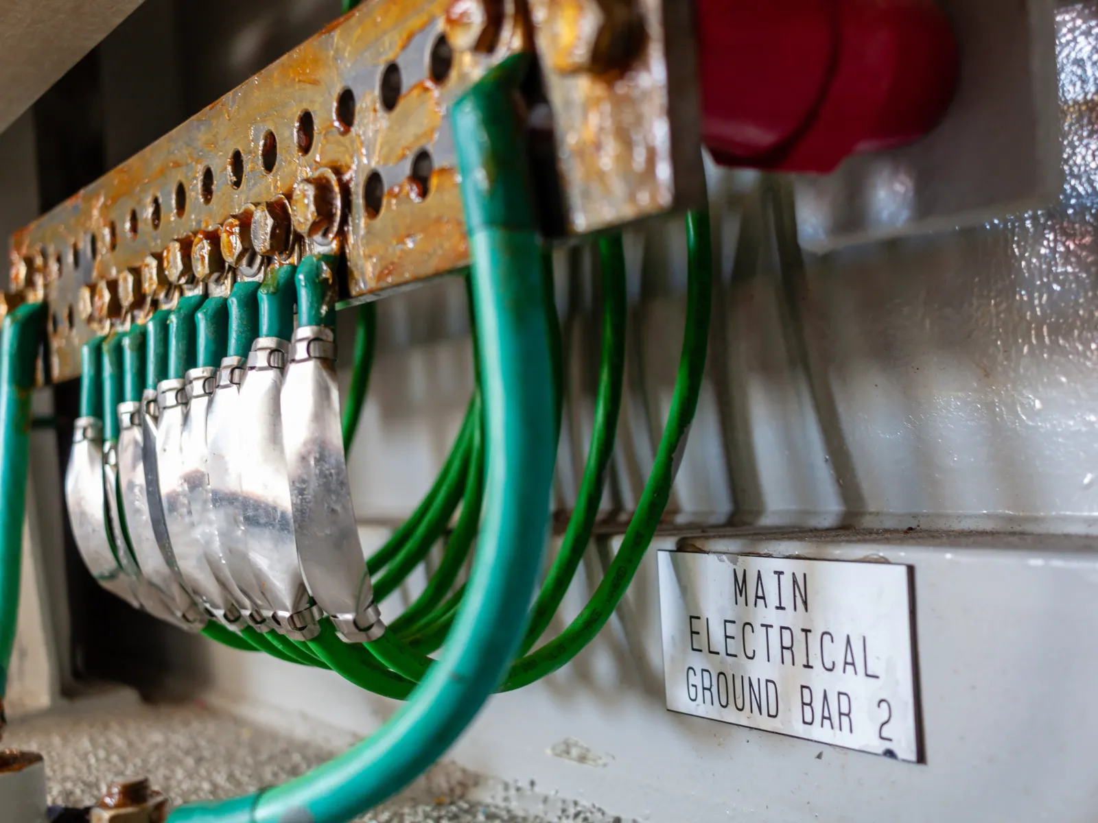 Electrician in a white hard hat and safety glasses working on an electrical panel with tools indoors.