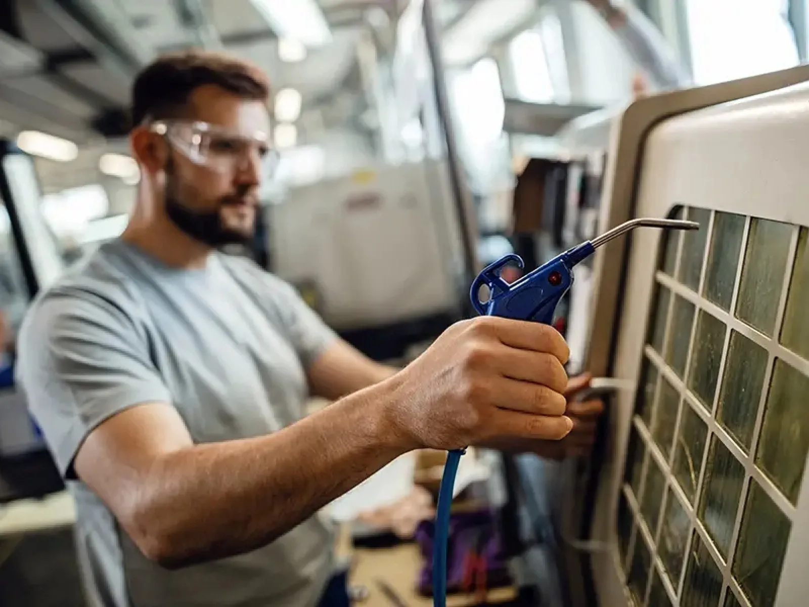 Man wearing safety glasses using an air blower to clean machinery in an industrial setting