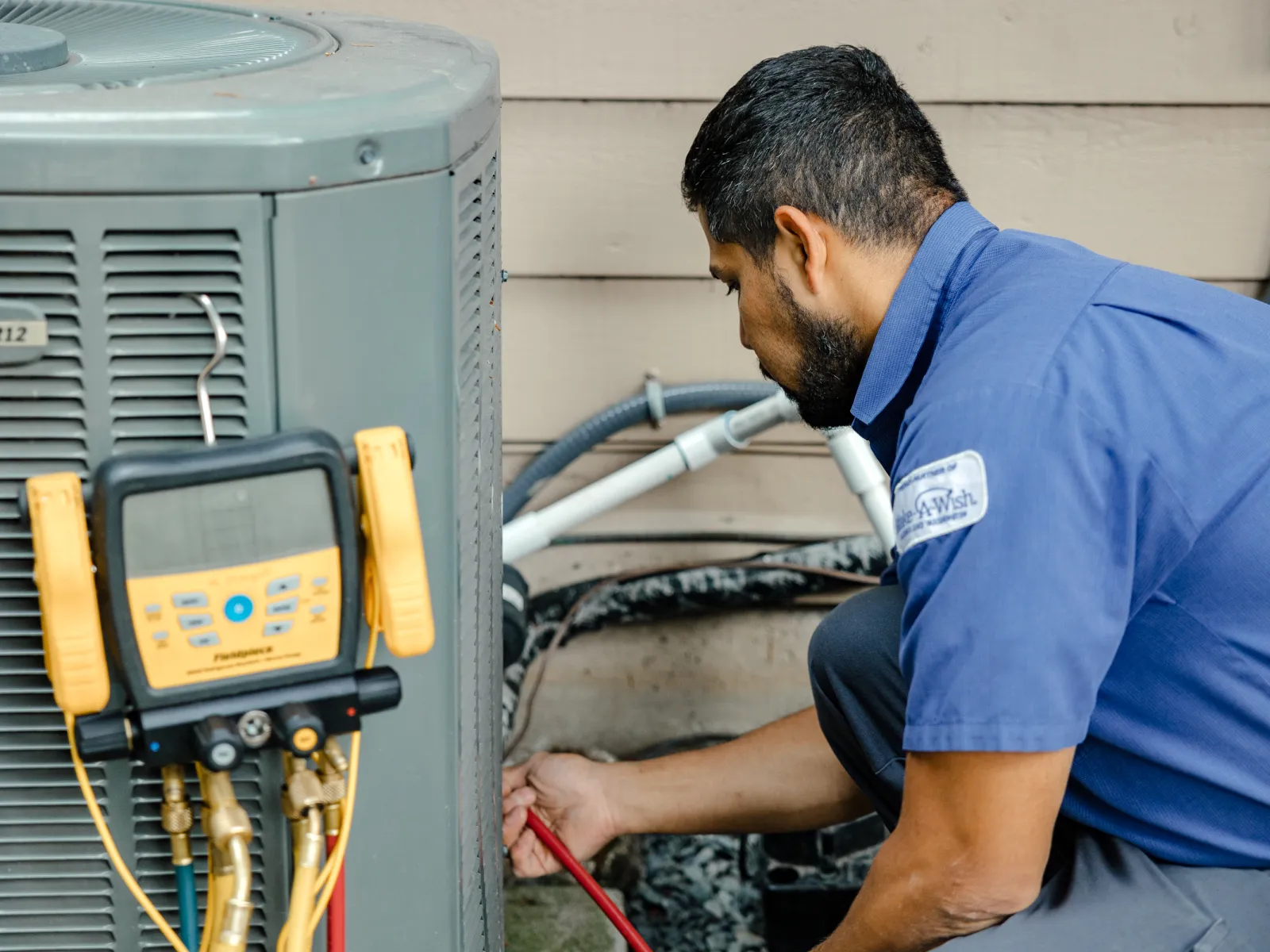 Technician in blue uniform inspecting and repairing residential air conditioning unit with diagnostic tools