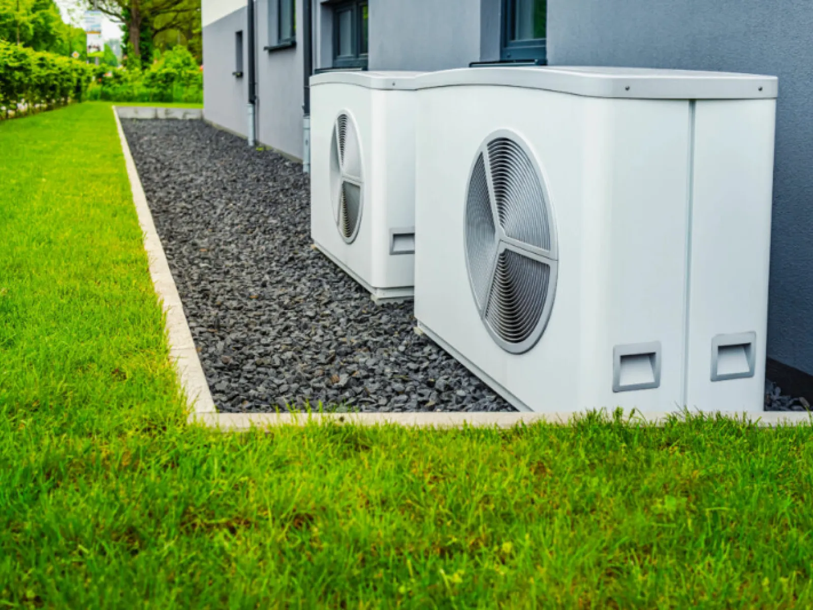 Two outdoor air conditioning units installed on gravel beside a modern house with green lawn.