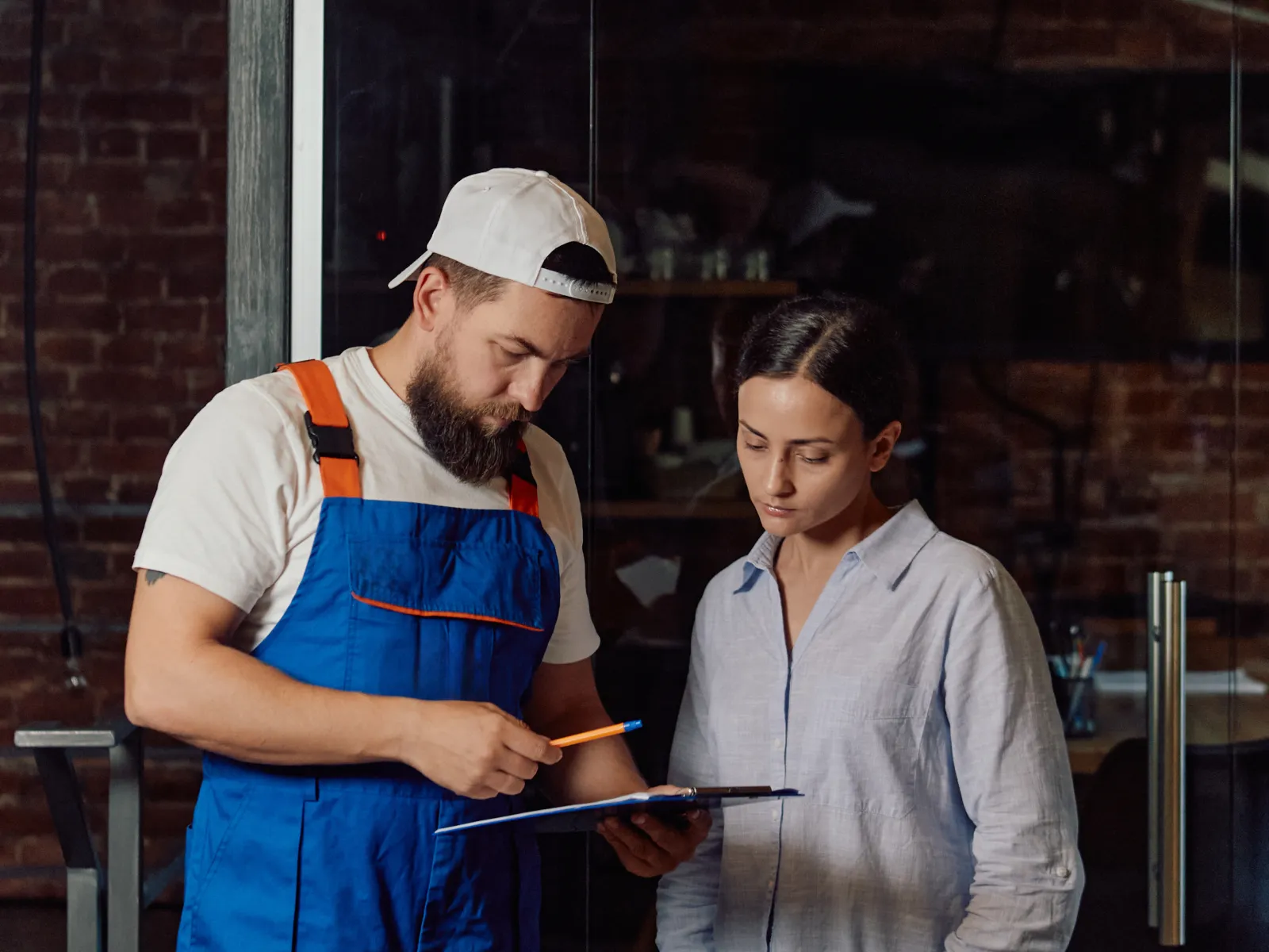 Technician in blue overalls consulting with woman in casual clothes under a ceiling air conditioning unit.