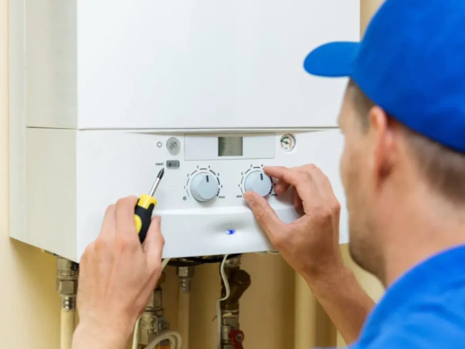 Technician adjusting temperature settings on a white boiler unit with a screwdriver indoors.